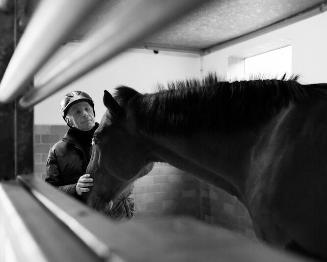 Schwarz-weiß Foto einer Person die ein Pferd im Stall streichelt