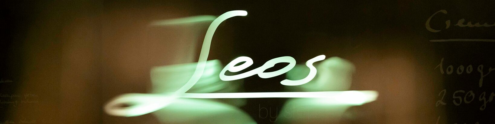 Leuchtschrift "Leos" in grünem Neonlicht vor dunklem Hintergrund