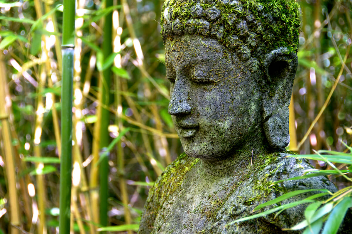 Moosbewachsene Buddha-Statue im grünen Garten des Bayerwaldhofs