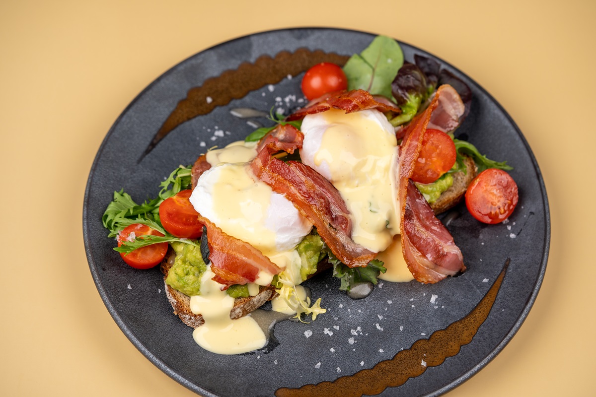 Herzhafte Brotzeit mit pochierten Eiern, Speck, Avocado und Tomaten auf dunklem Teller