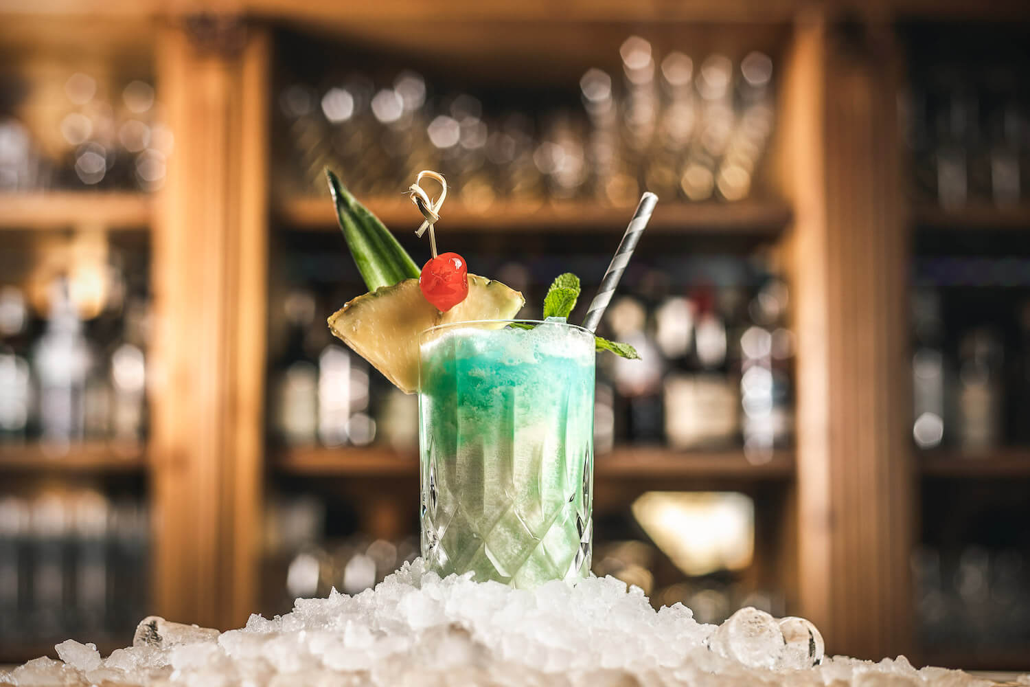 Blauer Cocktail mit Ananas und Kirsche auf Crushed Ice vor der Bar