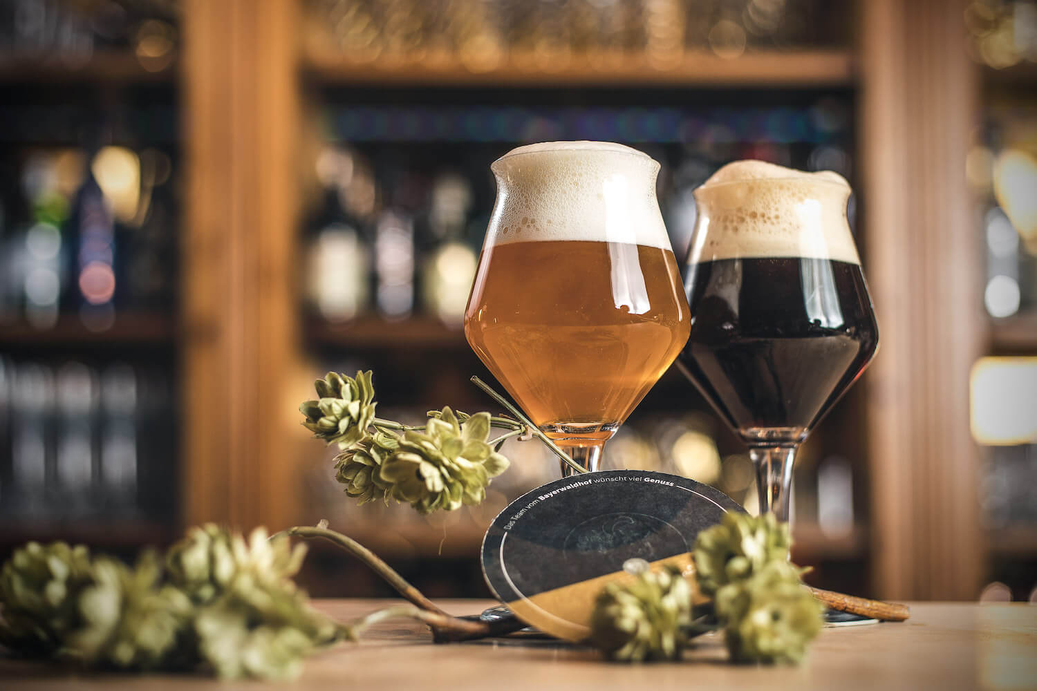 Zwei Biere im Glas mit Hopfendeko vor Barregal.