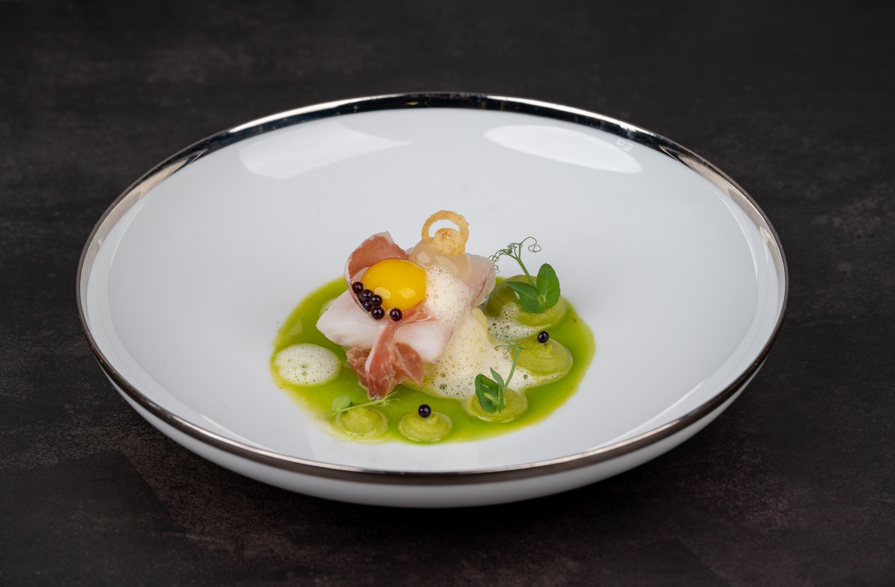 Kunstvoll angerichteten Vorspeise, bestehend aus Meeresfrüchten in grüner Sauce, garniert mit Kräutern und essbaren Blüten