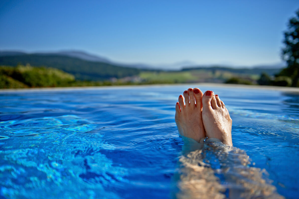 Füße am Poolrand mit Berglandschaft im Hintergrund