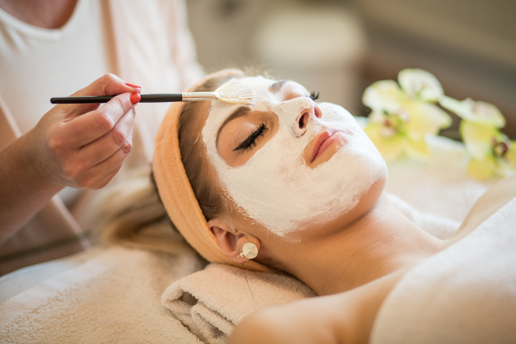Kosmetikerin trägt Maske auf Gesicht einer Frau auf