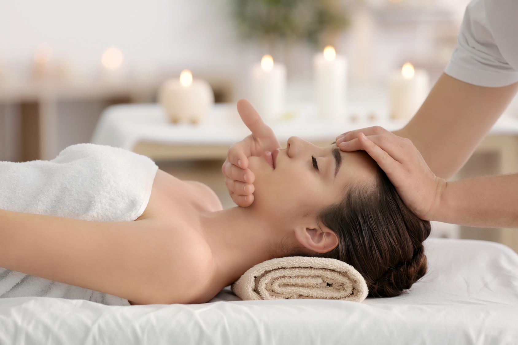 Massage mit Händen auf Kopf und Schultern einer Frau, Kerzen im Hintergrund