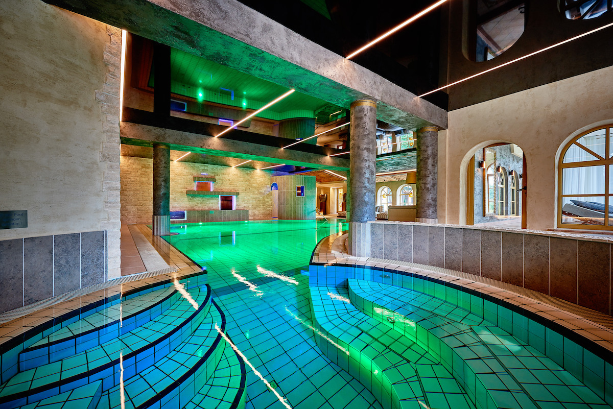 Relaxpool im Innenbereich mit grüner Beleuchtung, Steinbögen und modernem Design