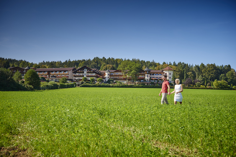 Bayerwaldhof-Gebäude mit grüner Wiese und Wanderern vor Waldkulisse