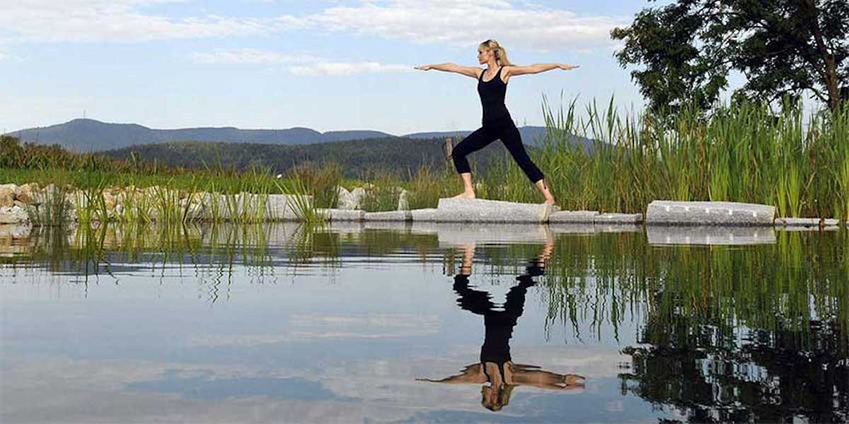 Frau in Yoga-Pose am Seeufer mit Bayerwald-Landschaft